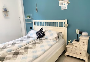 A bed with a checkered bedspread, a white headboard, and a nightstand with a lamp and a small plant.
