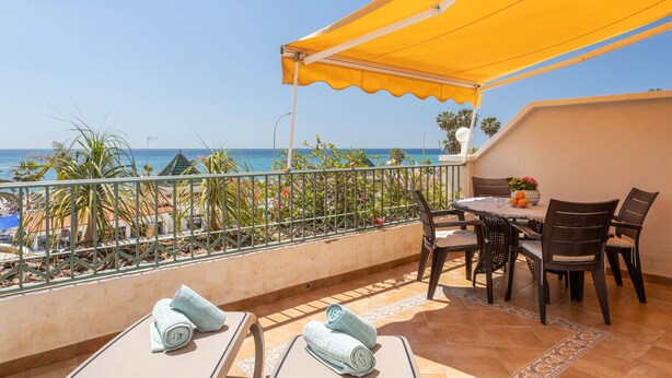 A balcony with a table and chairs, a yellow awning, and a view of the sea. - 'Sunny Apartment Front Line Burriana' Near the Beach with Sea View, Wi-Fi, A/C & Balcony (Nerja)