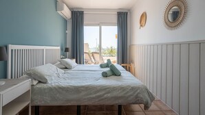 A bedroom with two beds, a window with curtains, a radiator, a wall-mounted mirror, and a view of the outside. - 'Sunny Apartment Front Line Burriana' Near the Beach with Sea View, Wi-Fi, A/C & Balcony (Nerja)