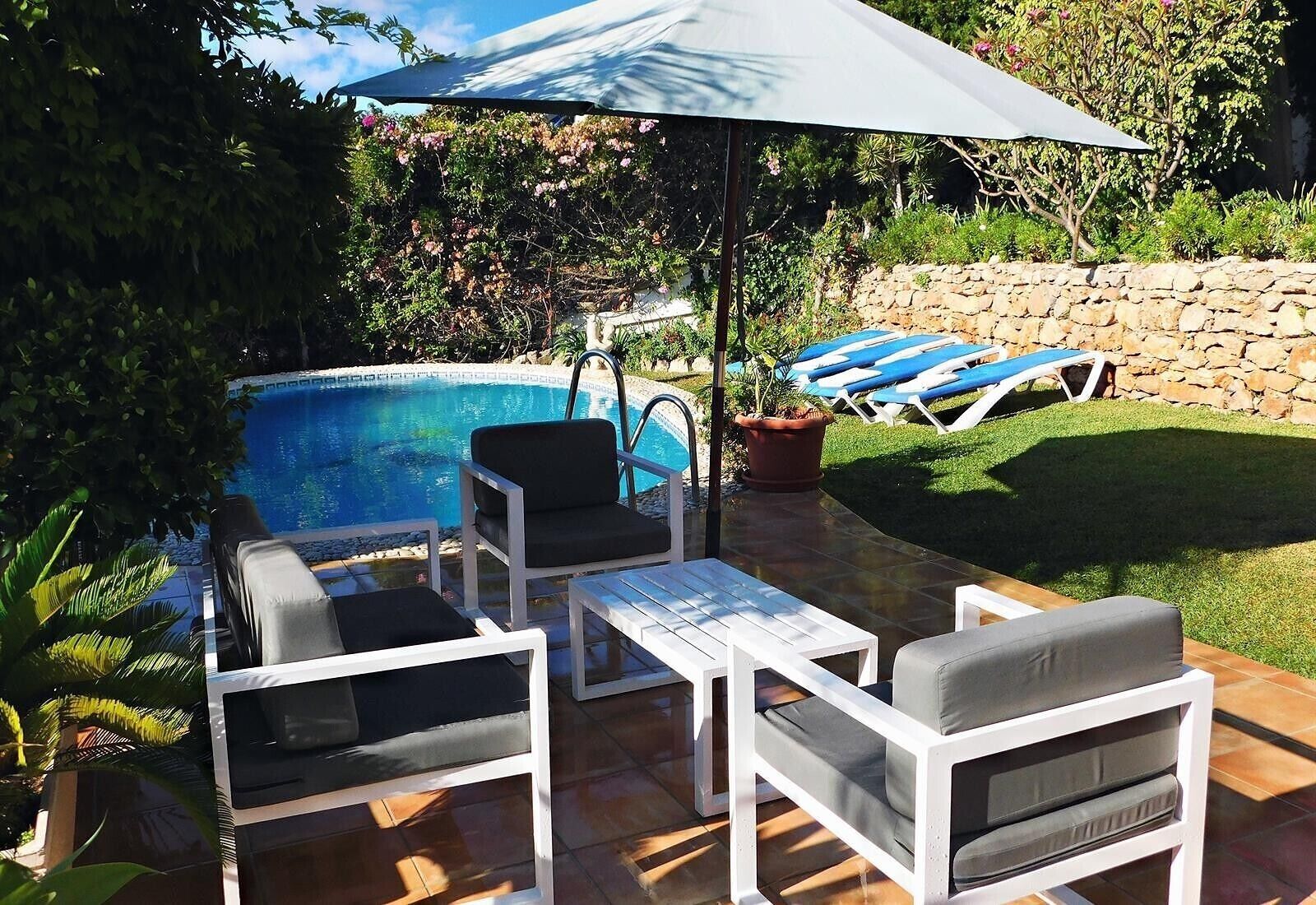 A poolside area with a pool, lounge chairs, a table, and an umbrella.