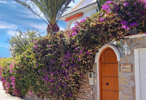 A villa with a stone wall, a wooden door, and a sign reading 'Villa Princesa 10'.