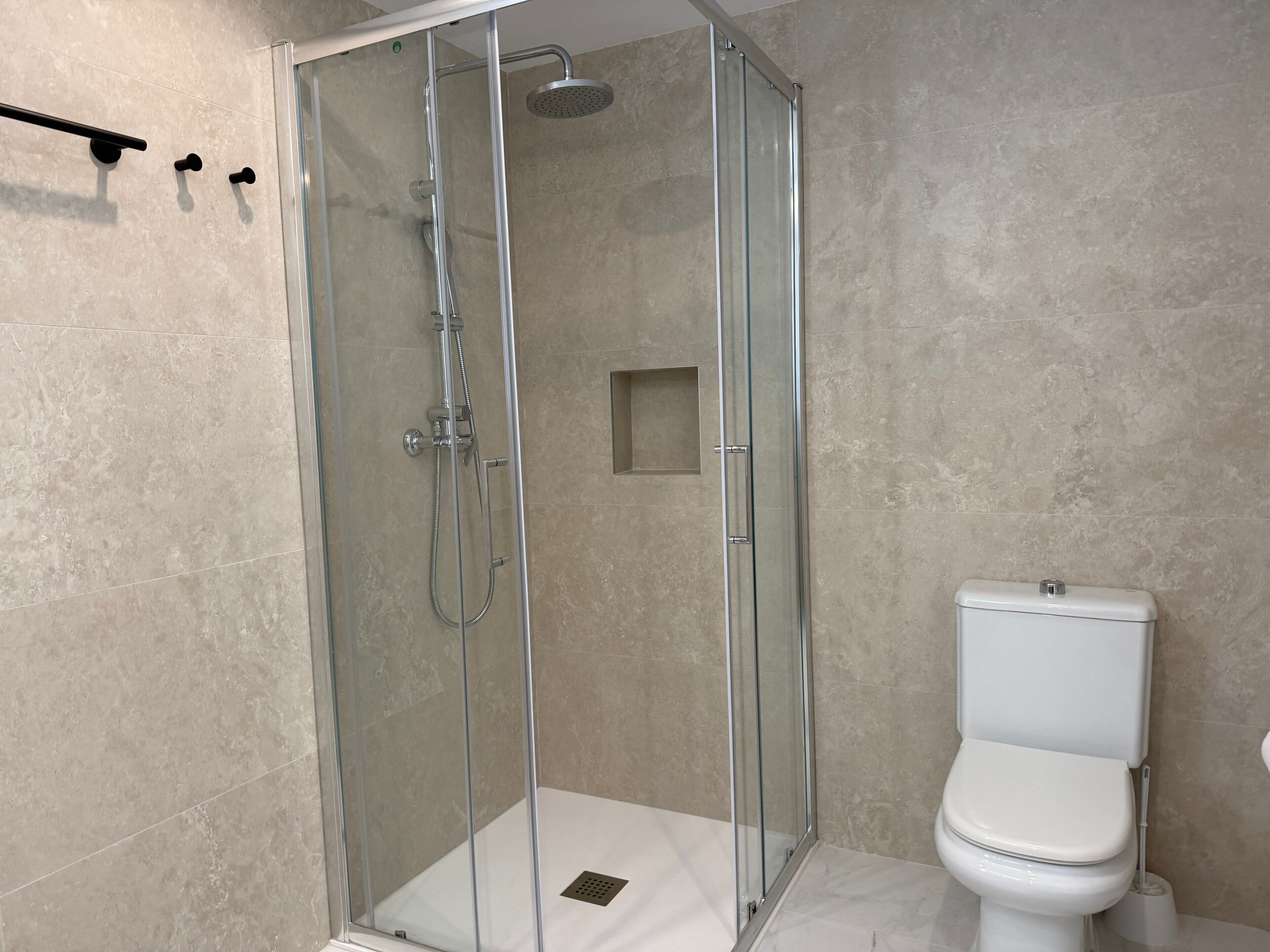 A glass-enclosed shower with a handheld showerhead and a wall-mounted faucet.
