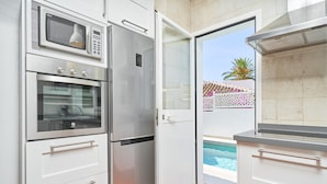 Una cuina amb forn integrat, microones i nevera, i una porta corredissa de vidre que dona a una zona de piscina.