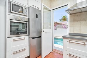 A kitchen with a built-in oven, microwave, and refrigerator, a sliding glass door leading to a pool area.