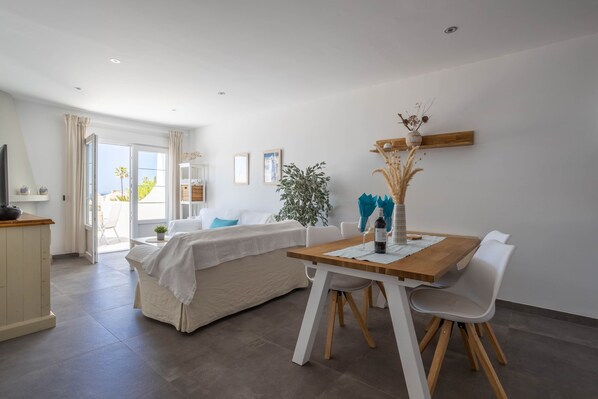 A modern room with a bed, a dining table with chairs, a small kitchen area, and a large window with curtains.