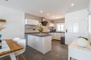 A modern kitchen with white cabinetry, a central island, and a dining area with a wooden table and white chairs.