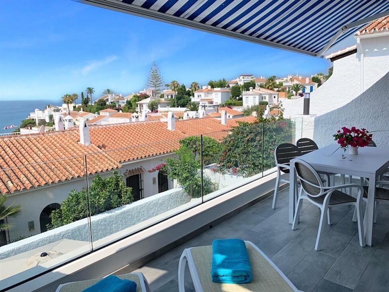 Un balcón con vistas a un pueblo costero, una mesa con sillas y una planta en maceta.