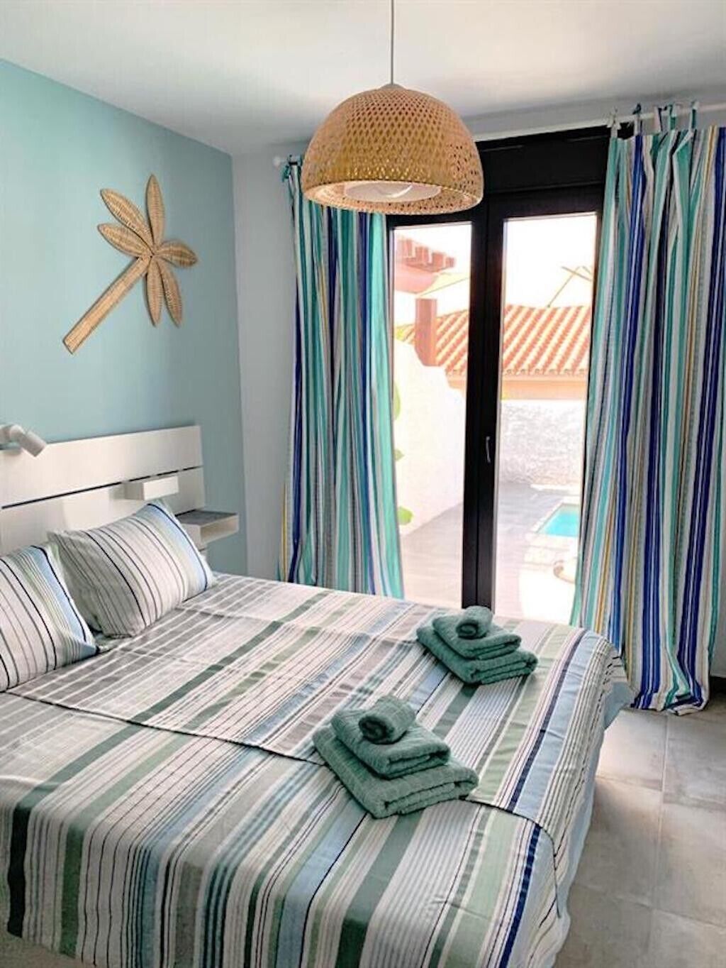 Un dormitorio con cama, lámpara colgante, ventana con cortinas y un adorno en la pared.