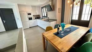 A modern kitchen with white cabinets, a built-in oven, and a dining area with a wooden table and chairs. - 'Wonderful House by the sea' with Sea & Mountain View, Pool and Wi-Fi (Nerja)