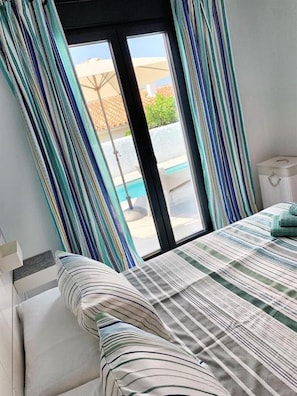 A bedroom with a bed, striped curtains, a window, and a view of an outdoor area.
