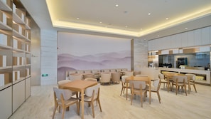 Un comedor moderno con mesas y sillas de madera, una zona de cocina con electrodomésticos de acero inoxidable y un mural de montañas en la pared.