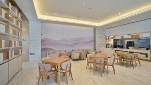 Zona pranzo moderna con tavoli e sedie in legno, angolo cottura con elettrodomestici in acciaio inossidabile e un murale raffigurante montagne sulla parete.