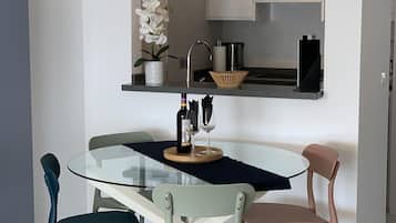 A modern kitchen with a glass dining table, two chairs, a potted orchid, and a wine bottle.
