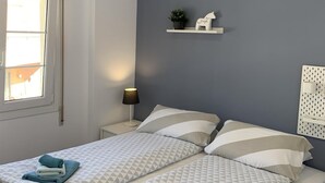 Een slaapkamer met een bed, nachtkastje, lamp, plank met een plant en decoratie, en een raam.