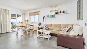 Un salon moderne comprenant un canapé, une table basse, une table à manger avec des chaises et un balcon avec des rideaux.