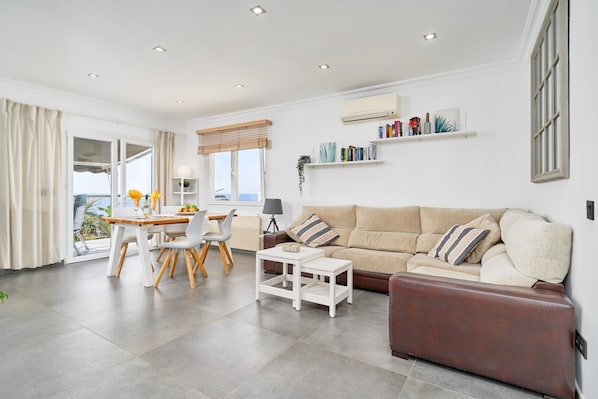 Un salon moderne comprenant un canapé, une table basse, une table à manger avec des chaises et un balcon avec des rideaux.