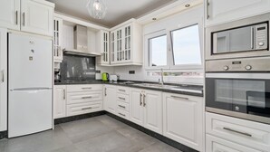 Une cuisine moderne avec des meubles blancs, un four encastré, un four à micro-ondes et une fenêtre au-dessus de l’évier.