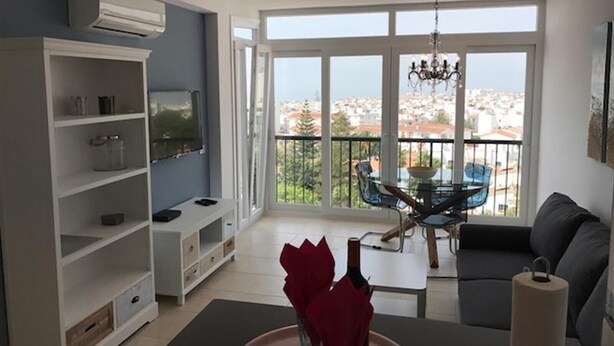 Un soggiorno con balcone, televisione e zona pranzo con tavolo e sedie.