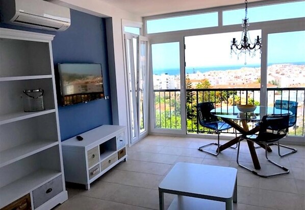 A balcony with a table and chairs, a TV on the wall, and a view of the city.