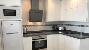 Una cucina con forno a microonde integrato, forno e piano cottura, mobili bianchi e paraschizzi in piastrelle.