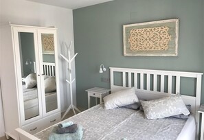 A bedroom with a bed, a wardrobe, a bedside table, and a wall-mounted decorative piece.