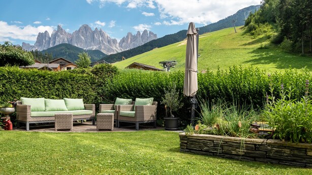 A patio with wicker furniture, a potted plant, and a stone planter. - Apartment 'Hilber Fermeda' with Mountain View, Private Terrace and Wi-Fi (Villnöss)