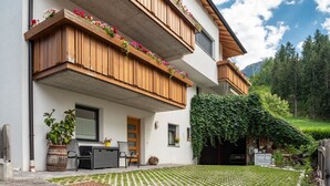 A two-story building with wooden balconies, a patio with outdoor furniture, and a garden area. - Apartment 'Hilber Fermeda' with Mountain View, Private Terrace and Wi-Fi (Villnöss)