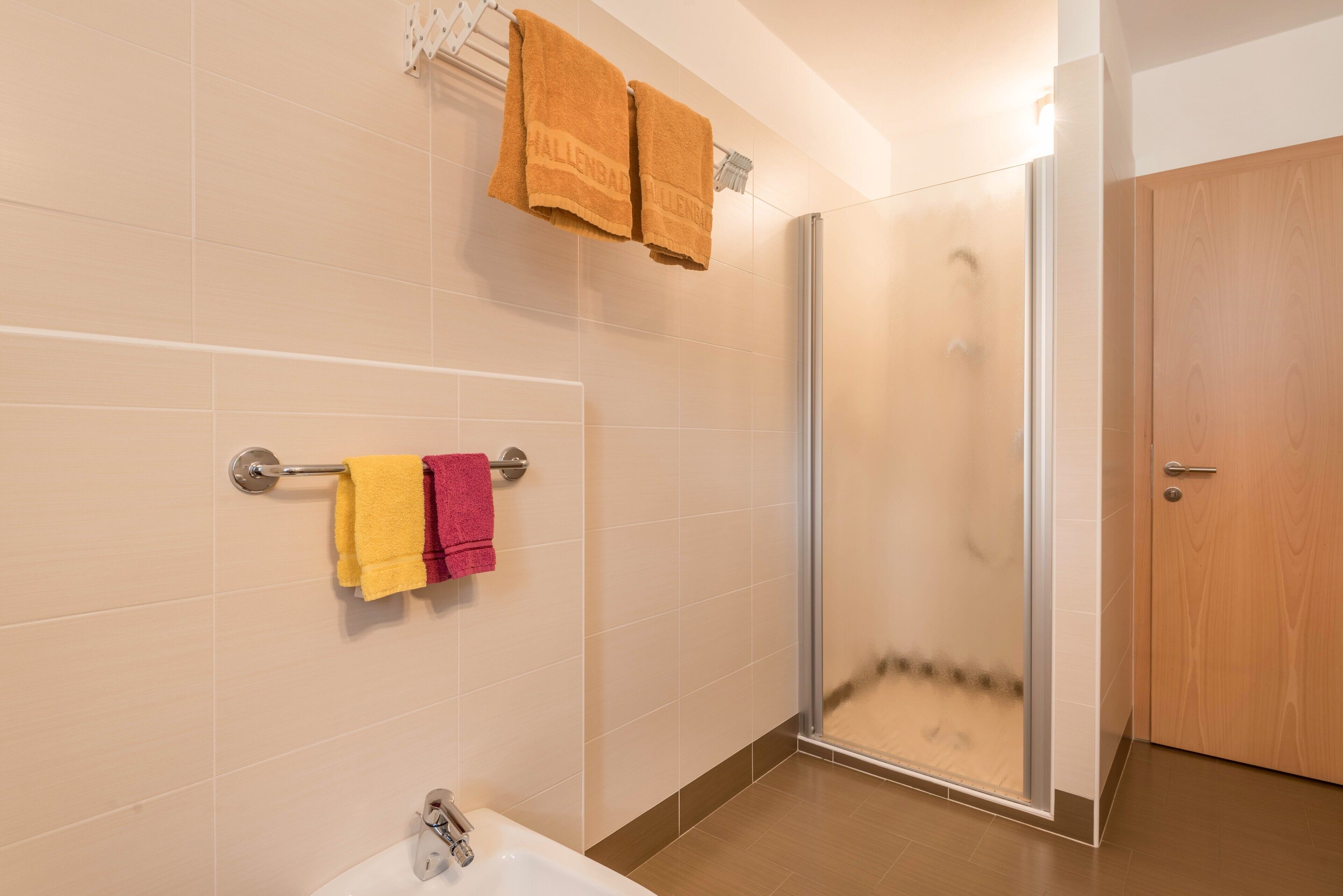 A bathroom with a shower, a sink, and towels on a rack.