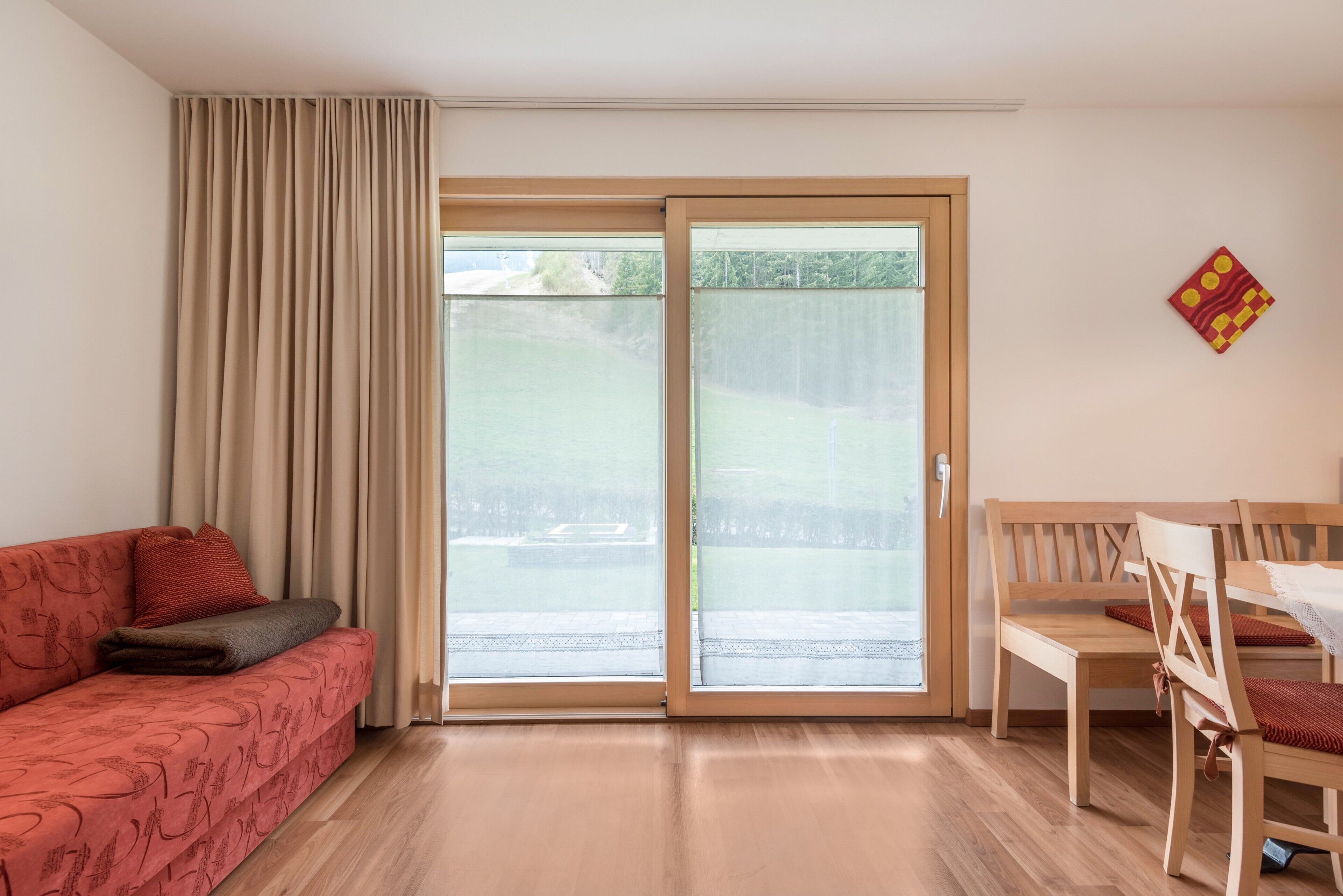 Ein Zimmer mit einer Schiebeglastür, einem roten Sofa, einem Holzessttisch und einem Stuhl.