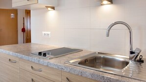 A modern kitchen with a built-in induction cooktop, stainless steel sink, and wooden cabinetry. - Apartment "Hilber Furchetta" with Mountain View, Garden and Wi-Fi (Villnöss)