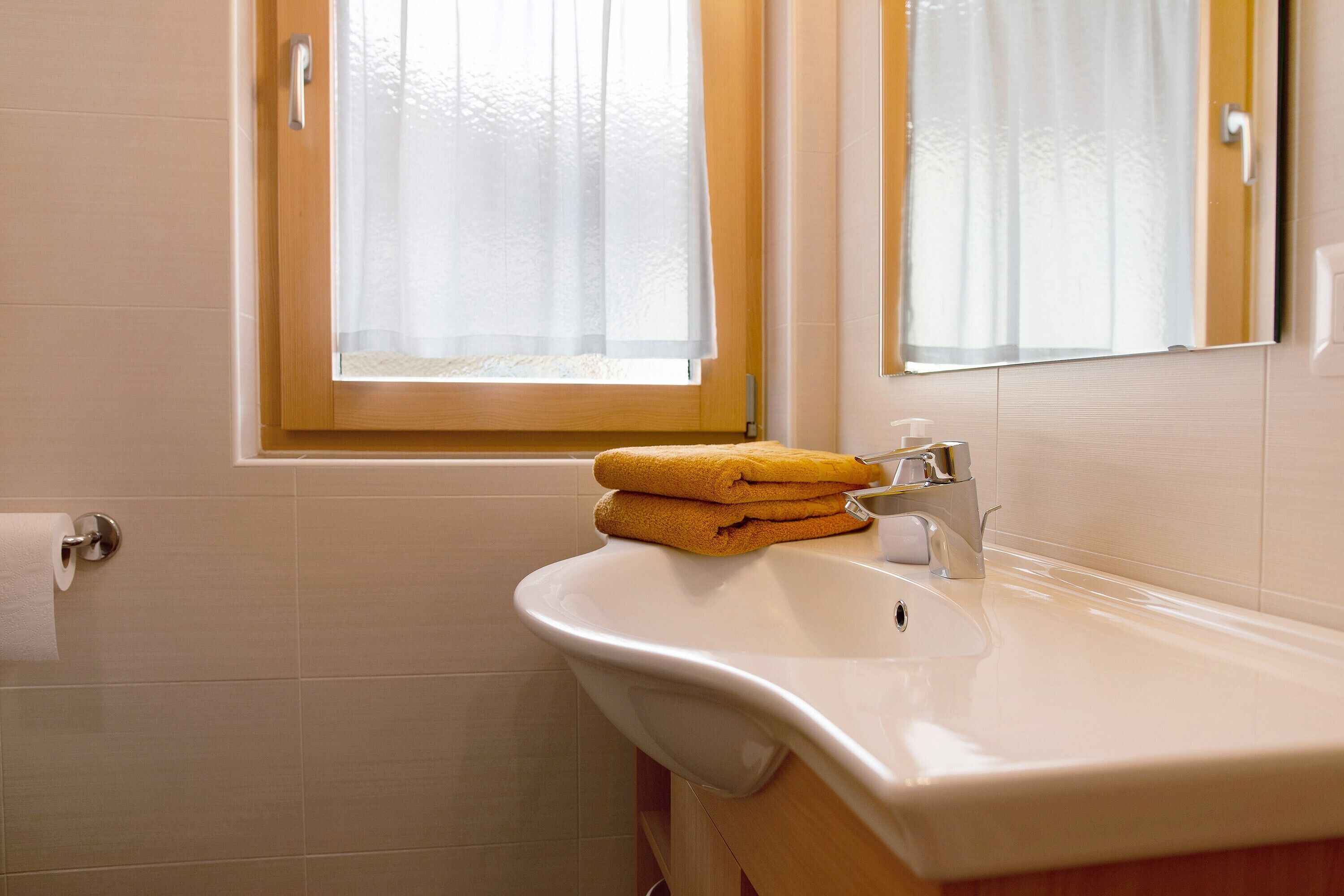 A bathroom with a sink, a towel rack, and a window with curtains.