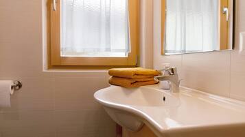 A bathroom with a sink, a towel rack, and a window with curtains.