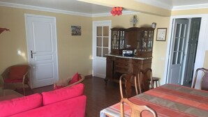 Un coin repas avec une table dressée pour quatre personnes, un canapé rouge, un fauteuil en osier et un buffet en bois doté de portes en verre.