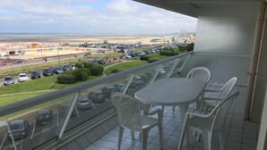 Un balcon avec une table et des chaises, donnant sur un parking et une plage.