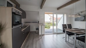 Une cuisine moderne dotée d’appareils électroménagers intégrés, un coin repas avec une table et des chaises, et une vue sur l’extérieur grâce à de grandes portes-fenêtres coulissantes.