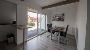 Une cuisine moderne dotée d’un four encastré, un coin repas avec une nappe à carreaux et une vue sur l’extérieur grâce à de grandes portes vitrées.