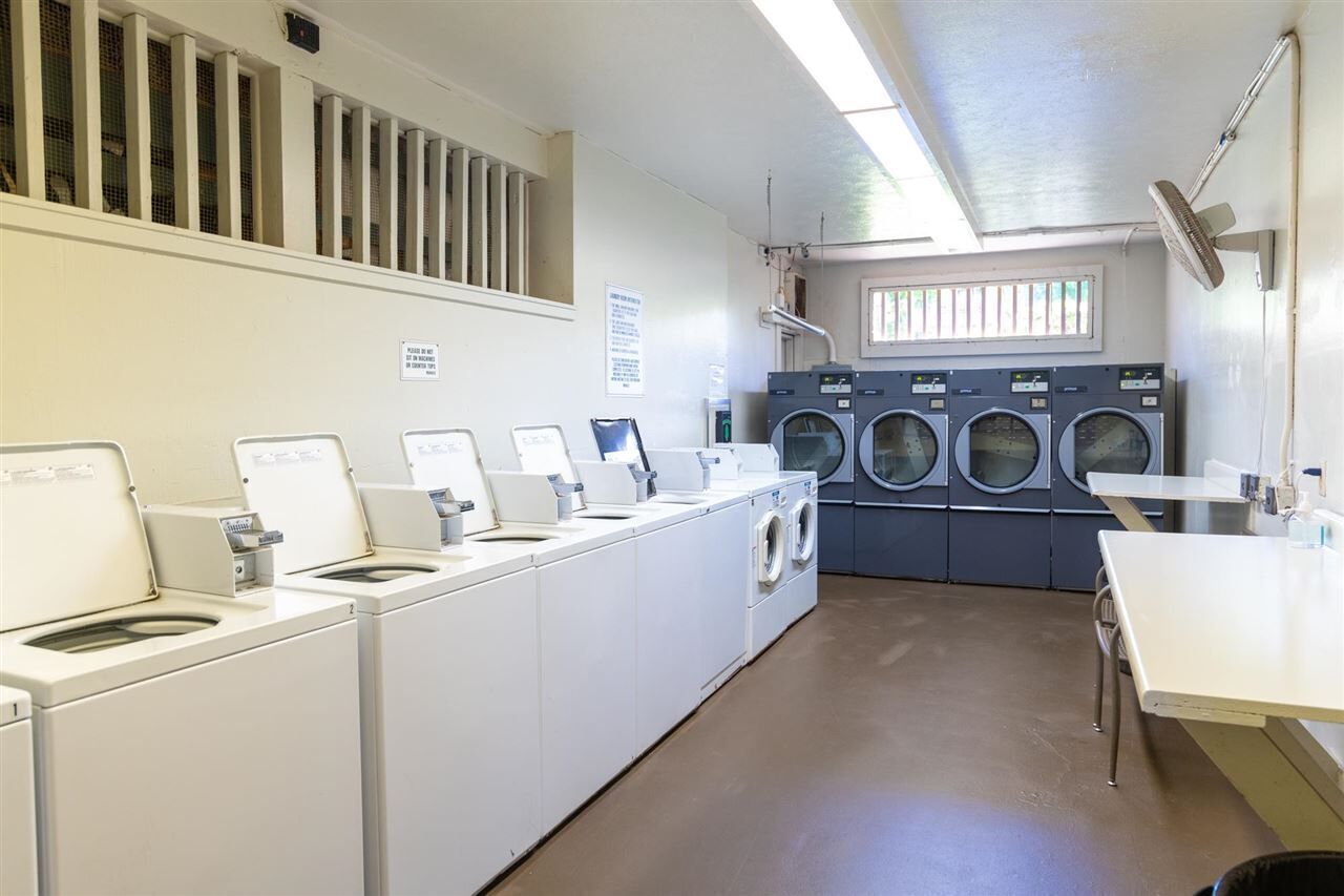 Ein Waschraum mit mehreren Waschmaschinen und Trocknern, einem Waschbecken und einem Tisch mit einem Ventilator.