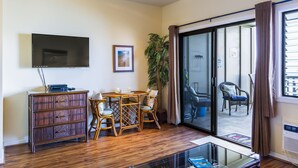 A living room with a flat-screen TV, a wooden cabinet, a dining table with chairs, a potted plant, and a sliding glass door leading to an outdoor area. - Direct Oceanfront Maui Studio,Romantic,Breathtaking View from Huge Private Lanai (Lahaina)