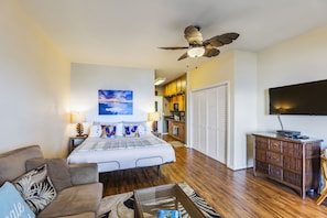 Une chambre d’hôtel avec un lit, un ventilateur de plafond, une télévision, une commode en bois et, au fond, un coin cuisine.