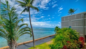 A coastal view with palm trees, a clear sky, and a building with a grey facade. - Direct Oceanfront Maui Studio,Romantic,Breathtaking View from Huge Private Lanai (Lahaina)