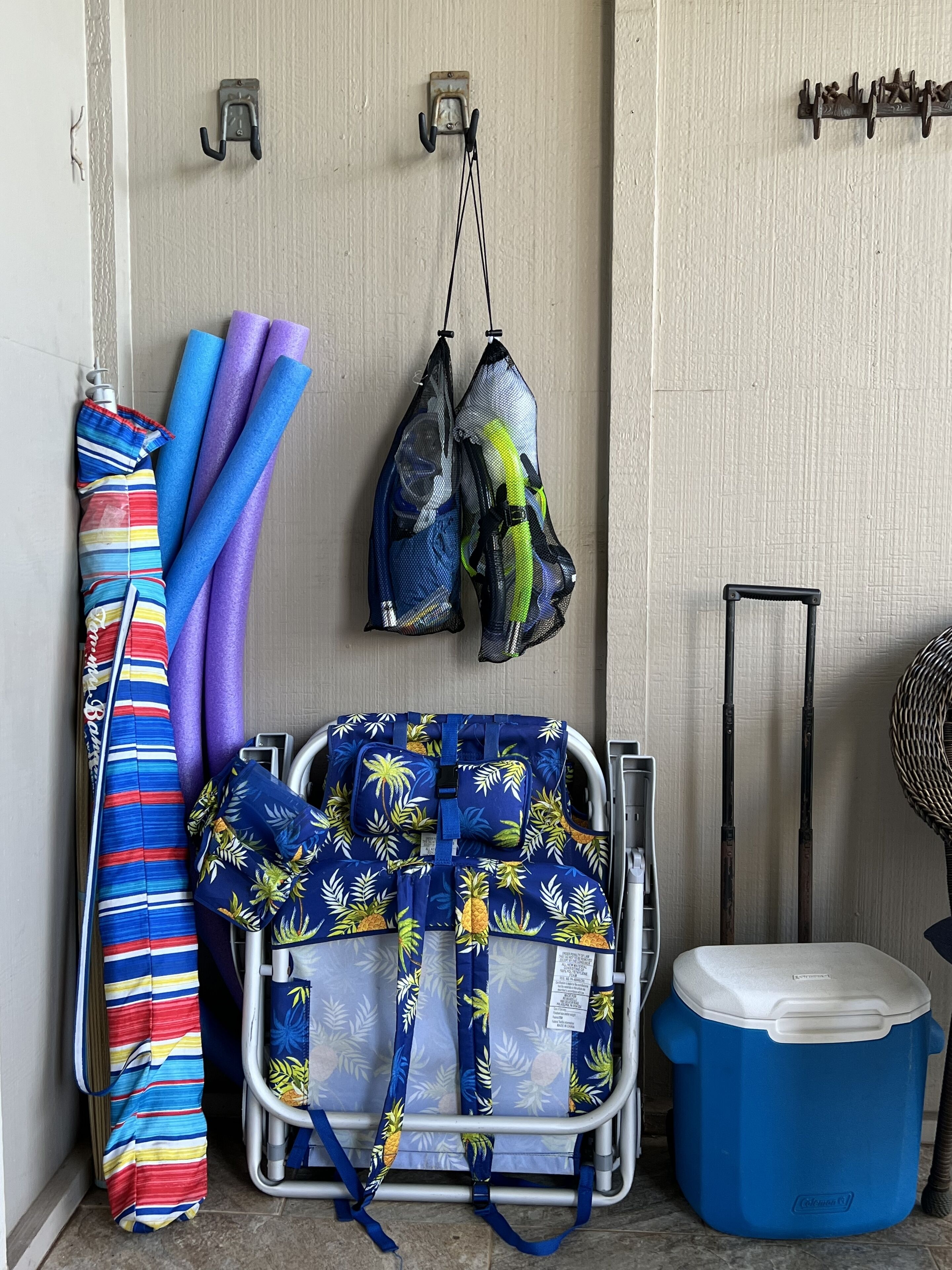 A room with a metal cart, a blue cooler, and colorful towels and bags hanging on hooks.