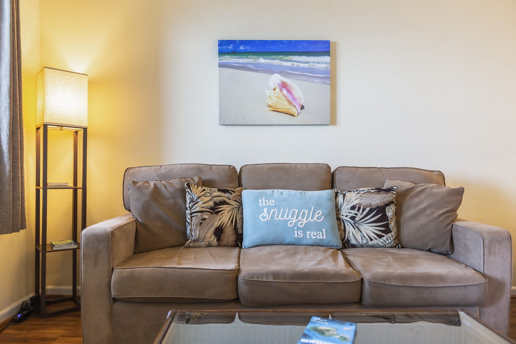Ein Dreisitzer-Sofa mit dekorativen Kissen, einer Stehlampe und einem gerahmten Bild von einer Strandlandschaft.