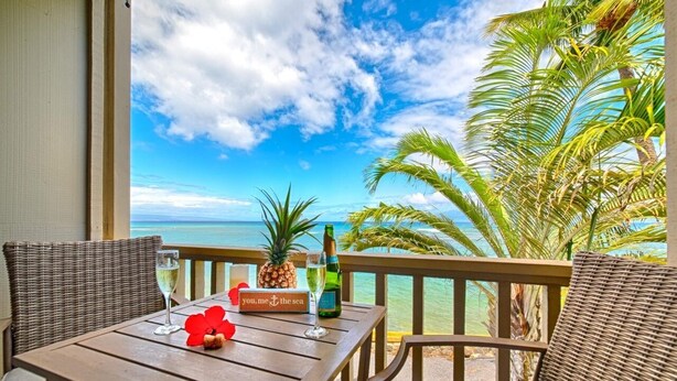 A wooden table with a bottle, a pineapple, a glass, and a sign on a balcony overlooking the sea. - Direct Oceanfront Maui Studio,Romantic,Breathtaking View from Huge Private Lanai (Lahaina)