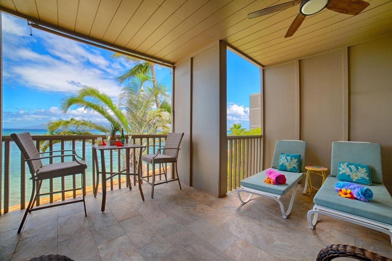 Un balcon avec vue sur l’océan, deux fauteuils en osier, une petite table et un fauteuil de relaxation avec un coussin.