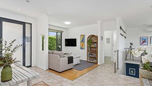 A living room with a sofa, a television, a bookshelf, and a staircase leading to another level. - 3 bedroom beachfront property - Stunning Ocean views - direct access to beach (Kiama Downs)