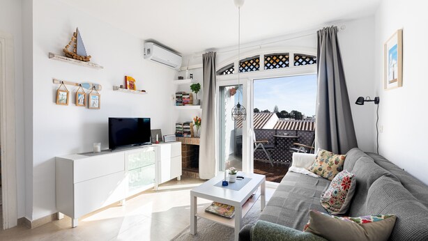 Een moderne woonkamer met een bank, salontafel en televisie. Er is een balkon met uitzicht op de stad.