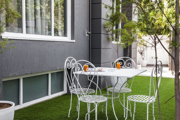 A patio with a white metal table and chairs, a small potted plant, and a window with a view of trees.