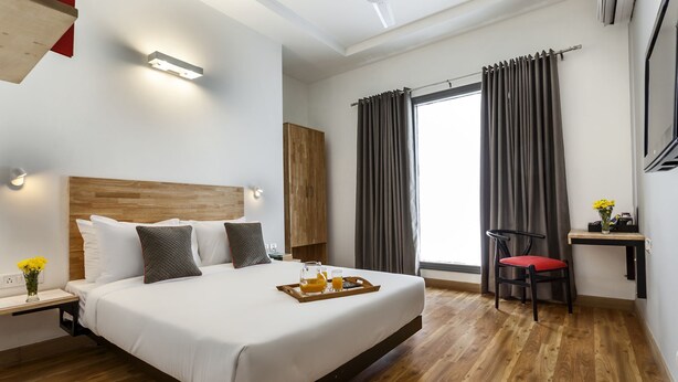 Una habitación de hotel con una cama grande, cabecera de madera, mesitas de noche con lámparas, un escritorio con una silla y una ventana con cortinas.