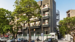 Un edificio de varios pisos con balcones, un árbol en la parte delantera y coches aparcados.