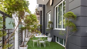 Un patio moderno al aire libre con una pequeña mesa y sillas, rodeado de macetas con plantas y un césped cuidado.